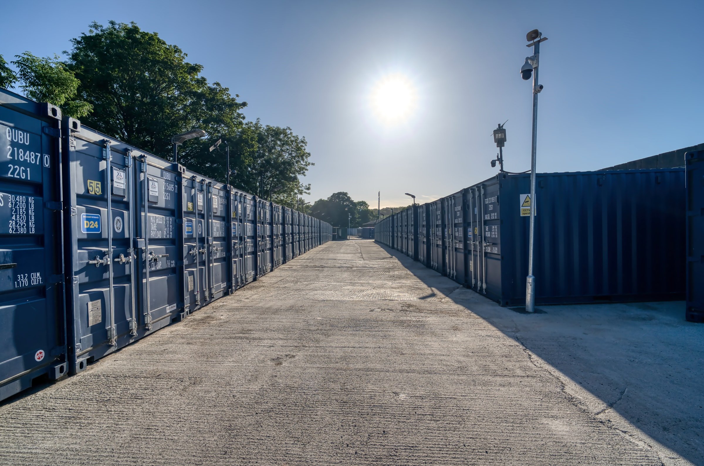 Low evening sunlight falling across the drive-up lane between storage container rows in Henbury
